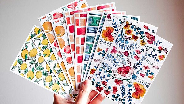 Eine Hand hält mehrere bunte Postkarten