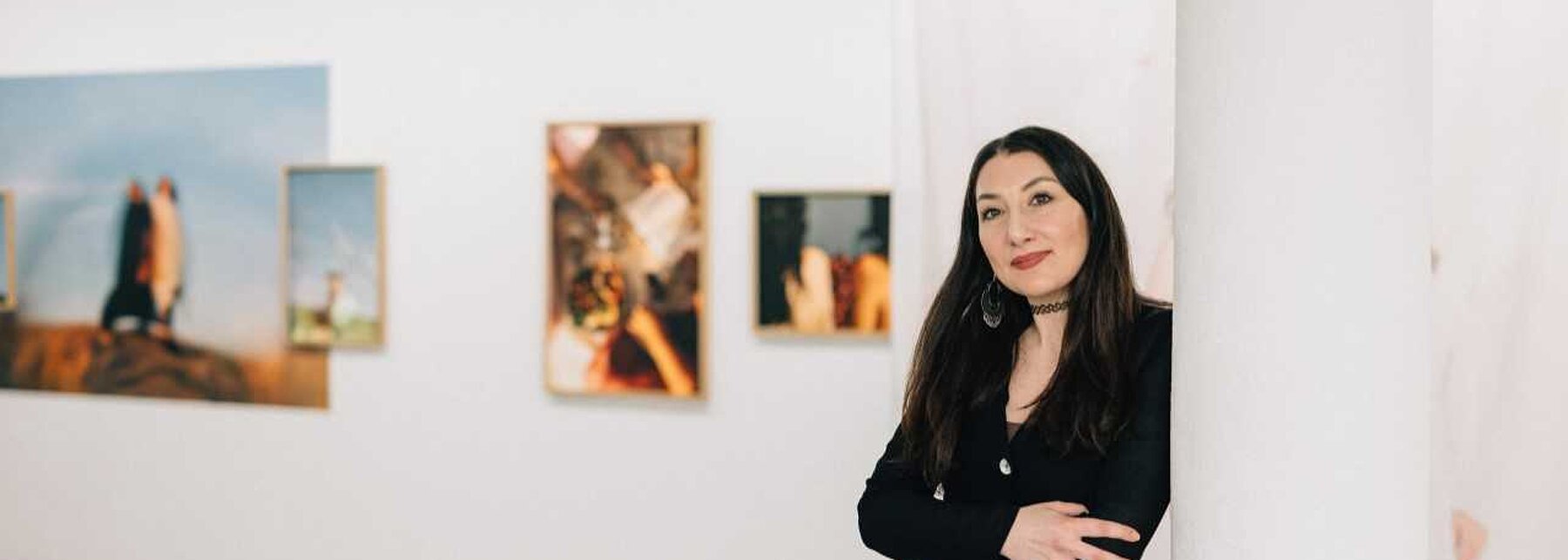 Frau lehnt an einer Wand mit Bildern im Hintergrund