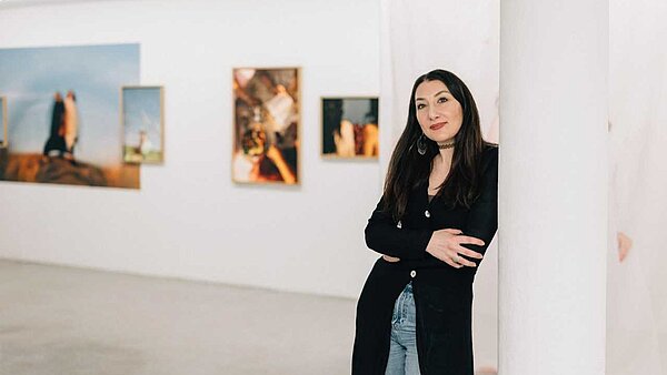 Frau lehnt an einer Wand mit Bildern im Hintergrund
