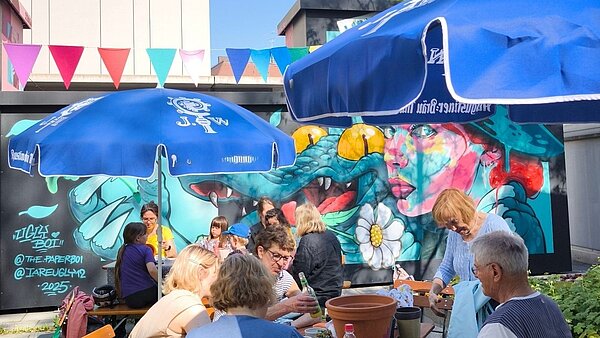 Menschen und Sonnenschirme vor Graffitiwand