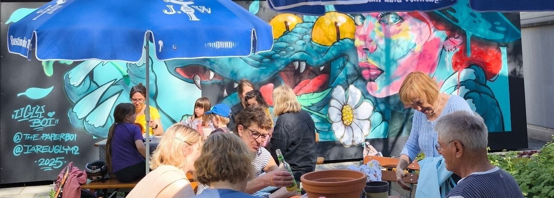 Menschen und Sonnenschirme vor Graffitiwand