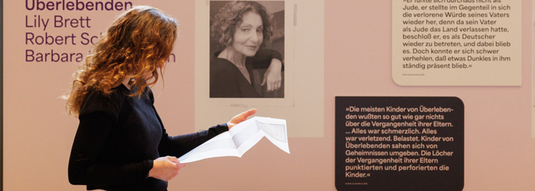 (c) Thomas Dashuber Frau schaut sich in einer Ausstellung Dokumente an, die in riesigen großen roten Ringordnern abgeheftet sind. Die Ordner liegen auf einem Tisch.
