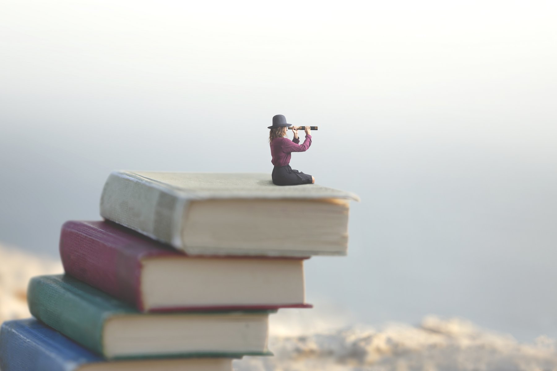 Frau sitzt auf überdimensioniertem Bücherstapel und blickt durch ein Fernrohr