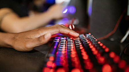 Eine Hand, die auf einer leuchtenden Tastatur liegt. 