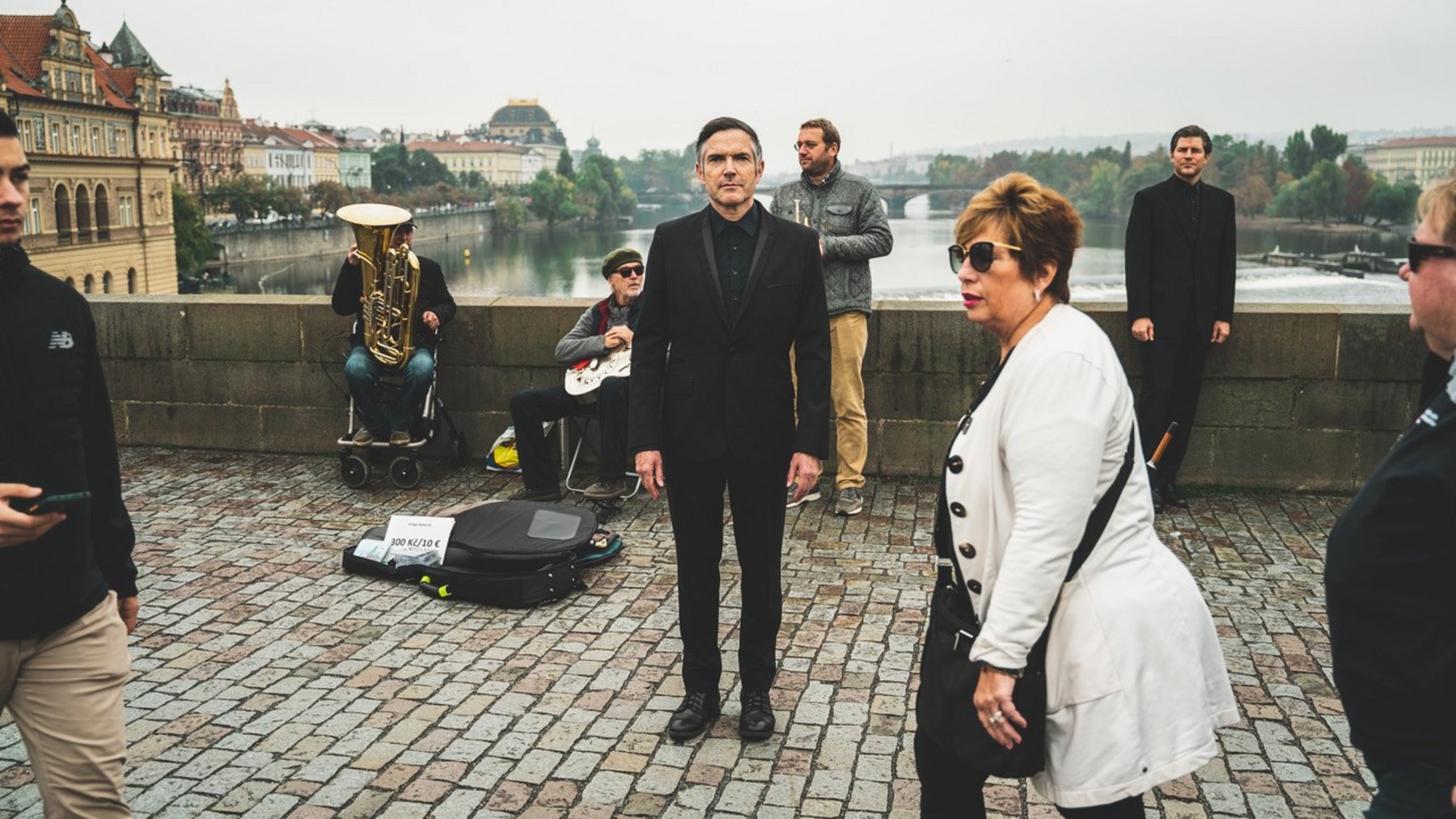 Eine Bandgruppe steht auf einer Brücke und performt. Im Vordergrund laufen andere Personen vorbei.