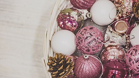 Weißer Korb auf hellem Holz mit rosa-weißen Weihnachtskugeln und einem Tannenzapfen.