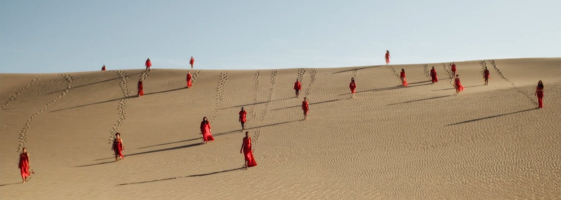 Frauen in roten Gewändern auf einer Düne