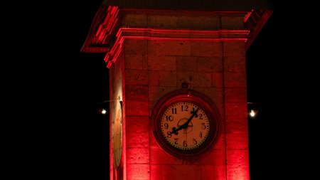 Ein Uhrturm bei Nacht der mit roten Schweinwerfern beschienen wird. 
