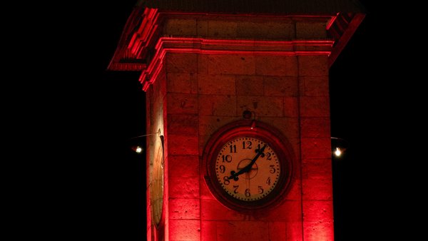 Ein Uhrturm bei Nacht der mit roten Schweinwerfern beschienen wird. 