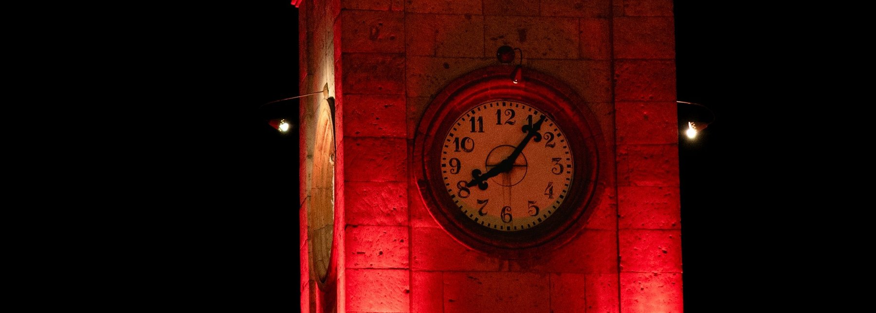 Ein Uhrturm bei Nacht der mit roten Schweinwerfern beschienen wird. 