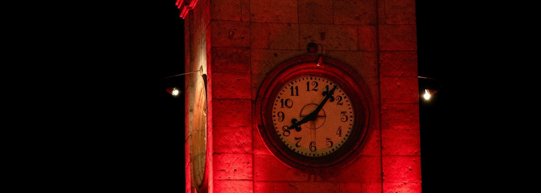 Ein Uhrturm bei Nacht der mit roten Schweinwerfern beschienen wird.