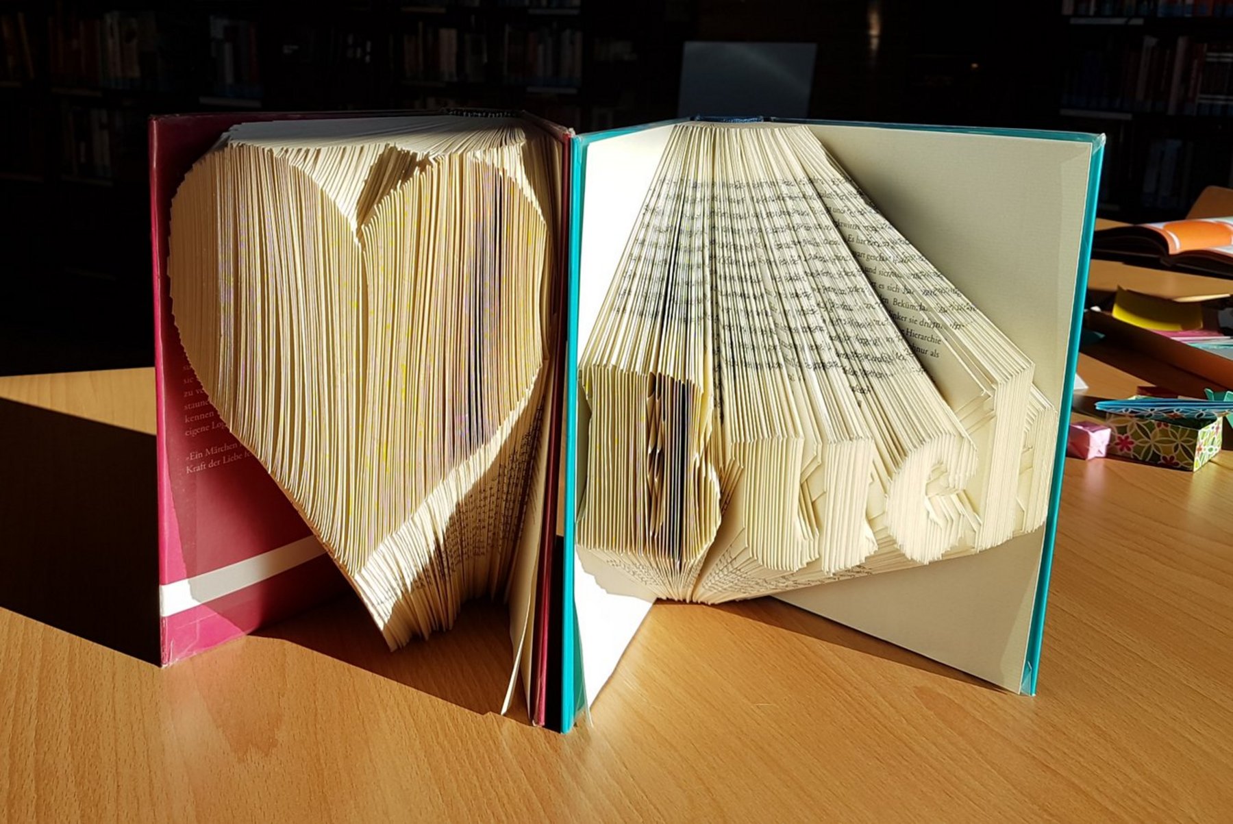 Zwei Bücher, deren Seiten gefaltet wurden. Ein Buch hat ein gefaltetes Herz, das andere das Wort "Buch".