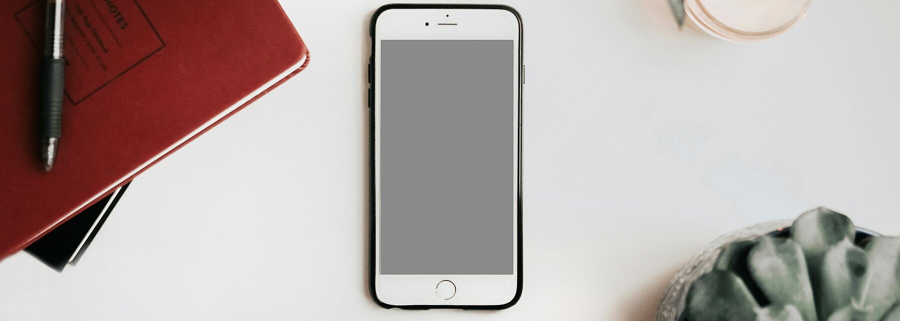 Ein Notizbuch, ein Smartphone und ein Teelicht auf einem Tisch.