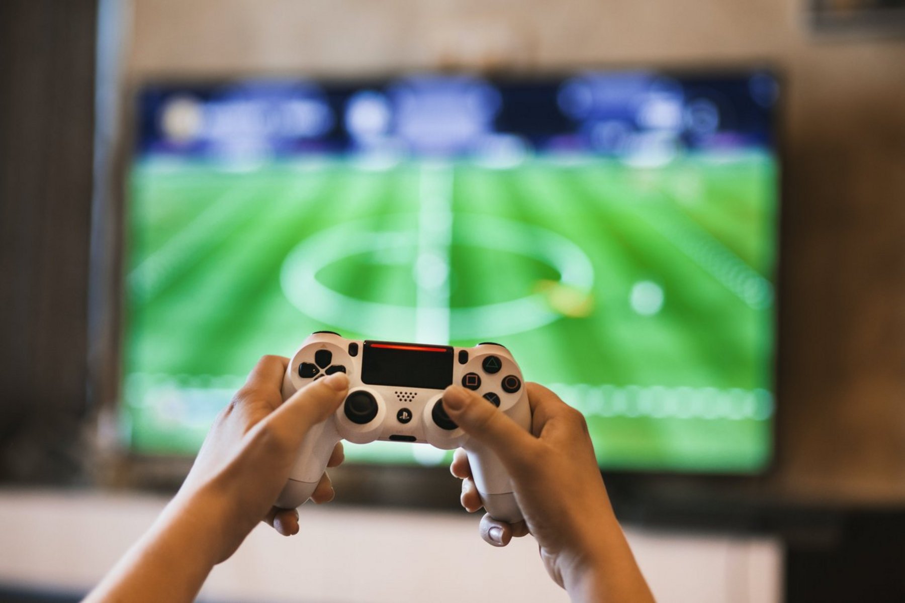 Playstation-Controller mit Fußball-Videospiel im Hintergrund