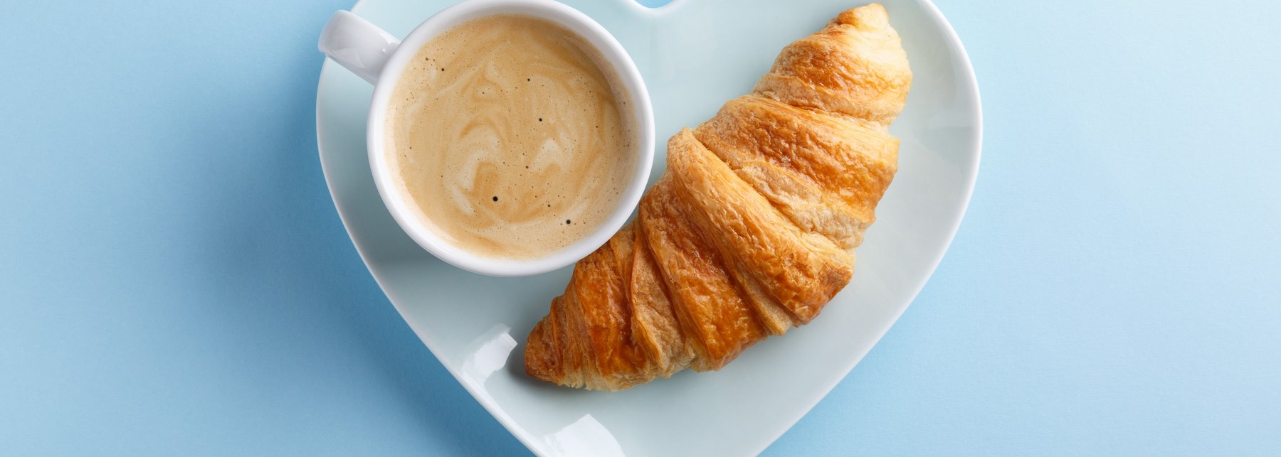 Eine Tasse Kaffee und ein Croissant auf einem herzförmigen Teller