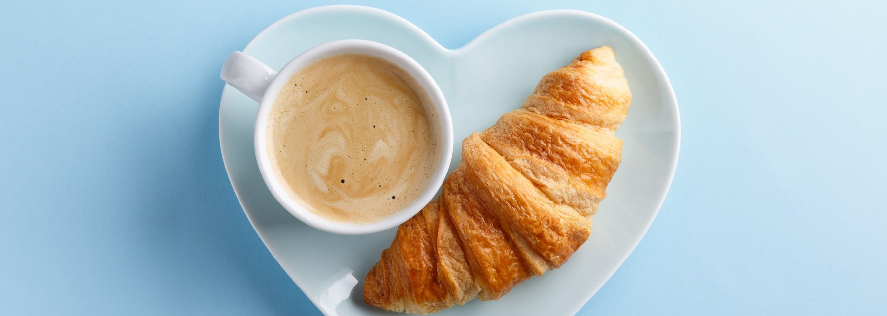 Eine Tasse Kaffee und ein Croissant auf einem herzförmigen Teller