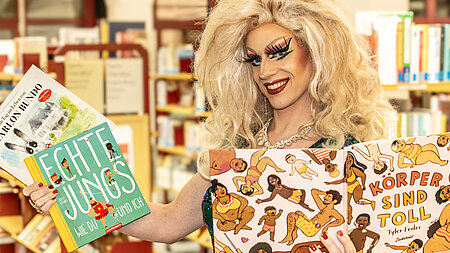 Drag-Queen hält Bilderbücher in der Hand