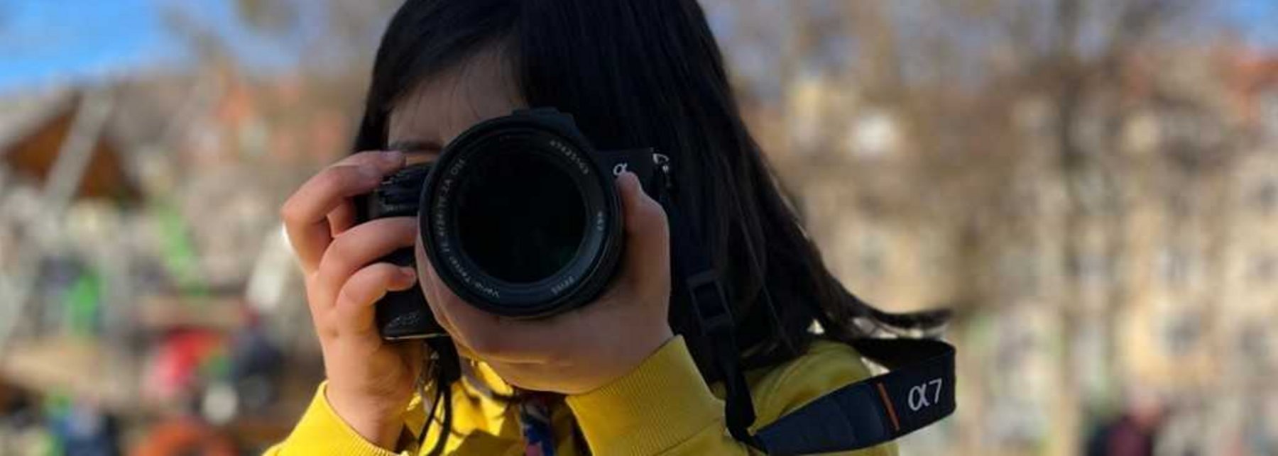 Kind mit Fotoapparat in gelber Jacke