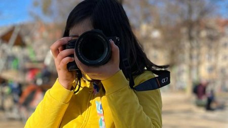 Kind mit Fotoapparat in gelber Jacke