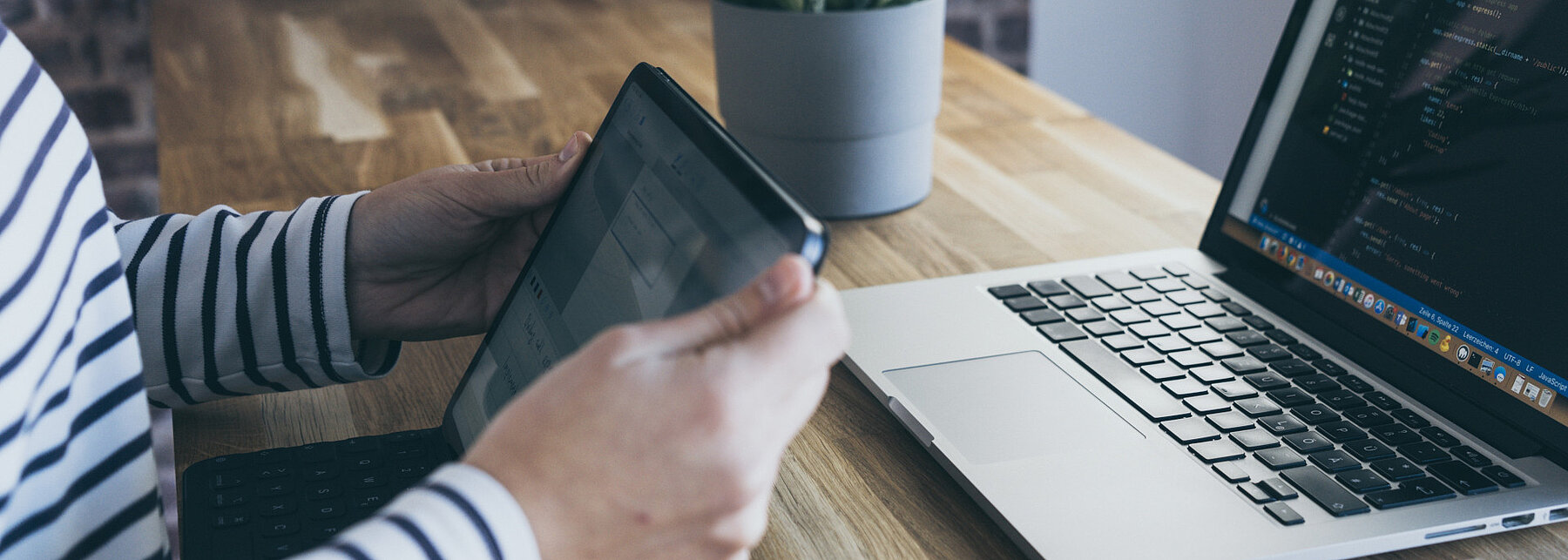 eine Person sitzt mit einem Tablet vor einem Laptop