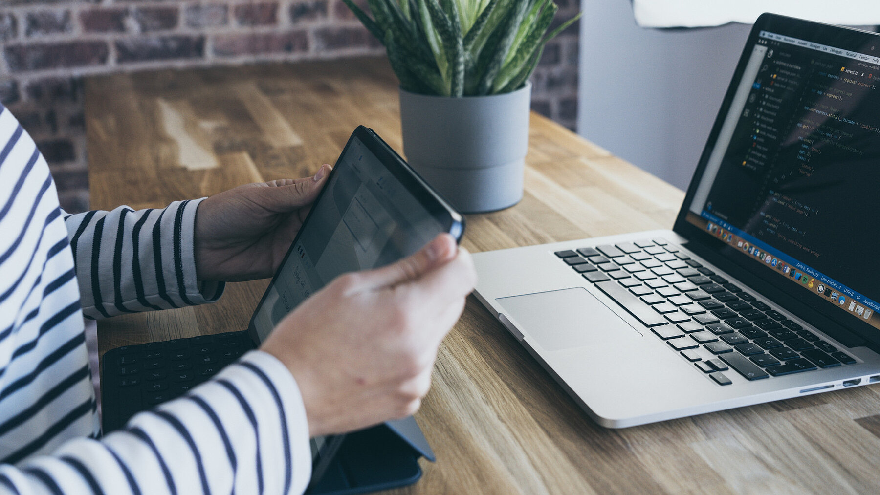 eine Person sitzt mit einem Tablet vor einem Laptop