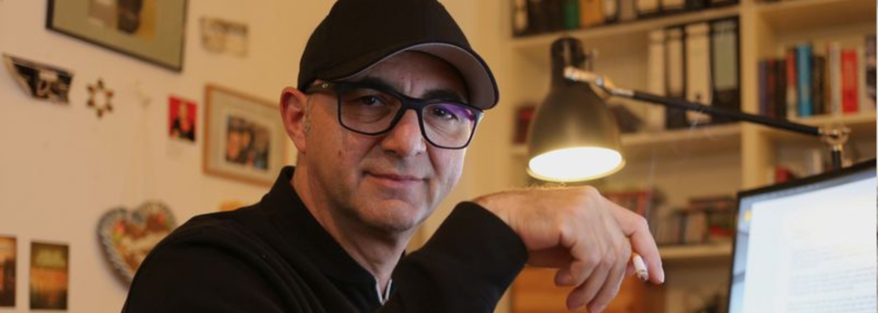 Su Turhan sitzt an seinem Schreibtisch und hält lässig mit der Hand eine Zigarette. Sehr gewagt auf einem Autorenportrait, aber auch sehr cool.