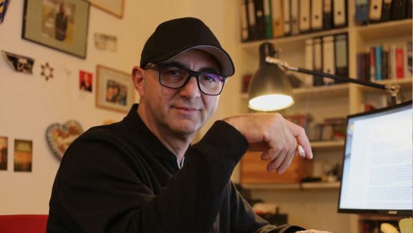 Su Turhan sitzt an seinem Schreibtisch und hält lässig mit der Hand eine Zigarette. Sehr gewagt auf einem Autorenportrait, aber auch sehr cool.