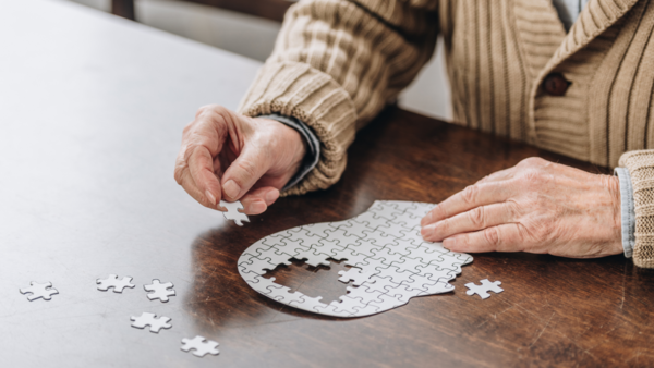 Eine ältere Person setzt ein Puzzle in Form eines Kopfes zusammen.
