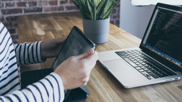 eine Person sitzt mit einem Tablet vor einem Laptop