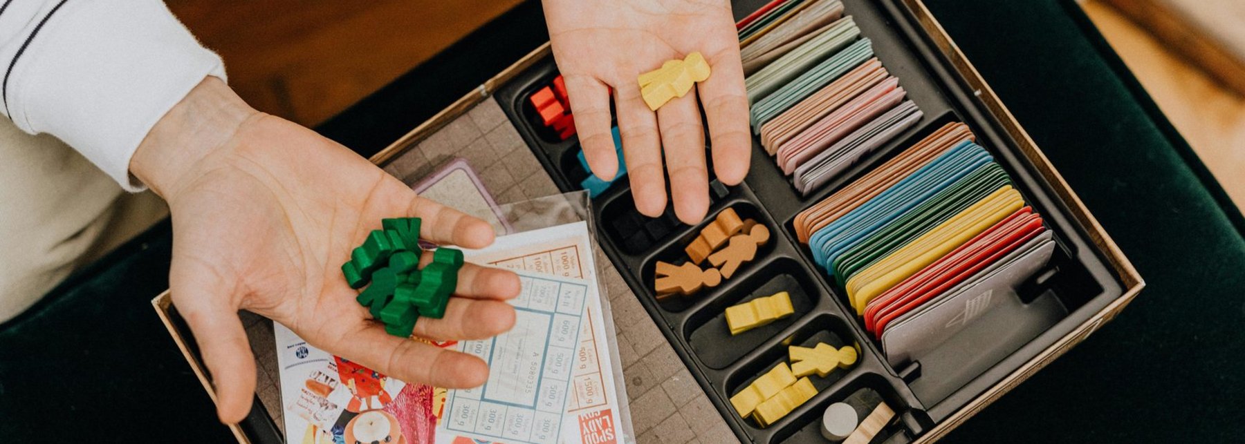 Hände mit Spielfiguren über einer offenen Brettspielverpackung