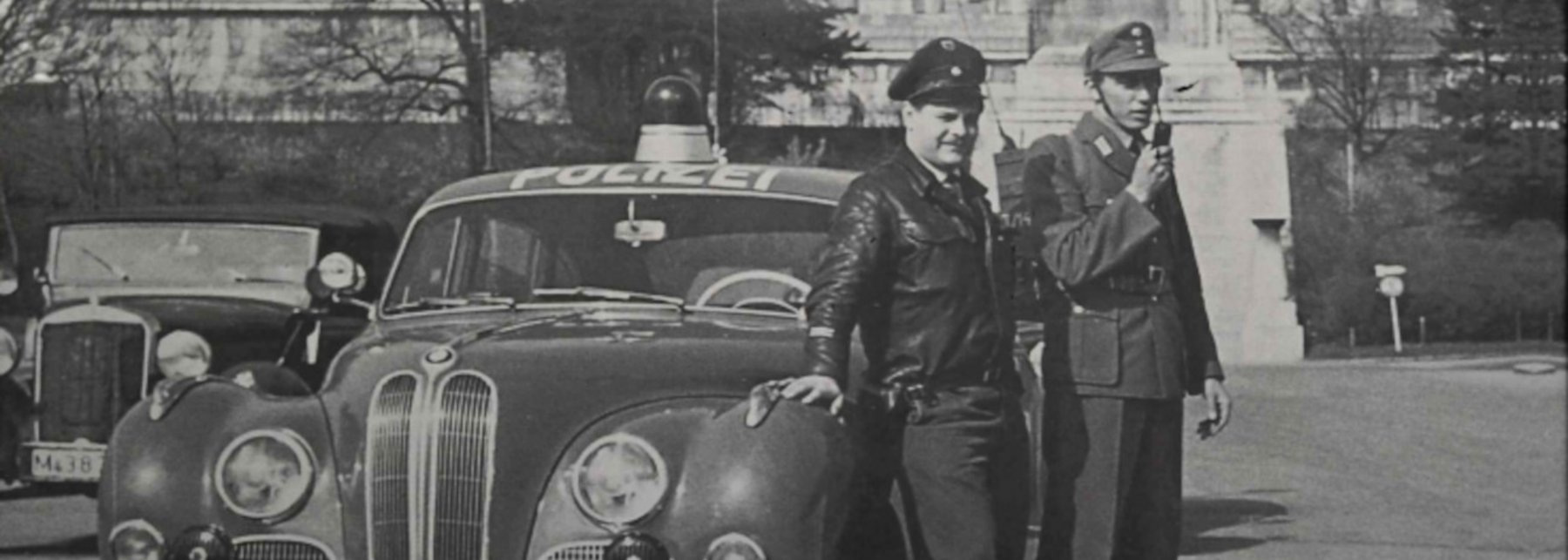 Schwarz-Weiß-Foto von zwei Polizisten vor einem Polizeiauto aus den 1950er Jahren